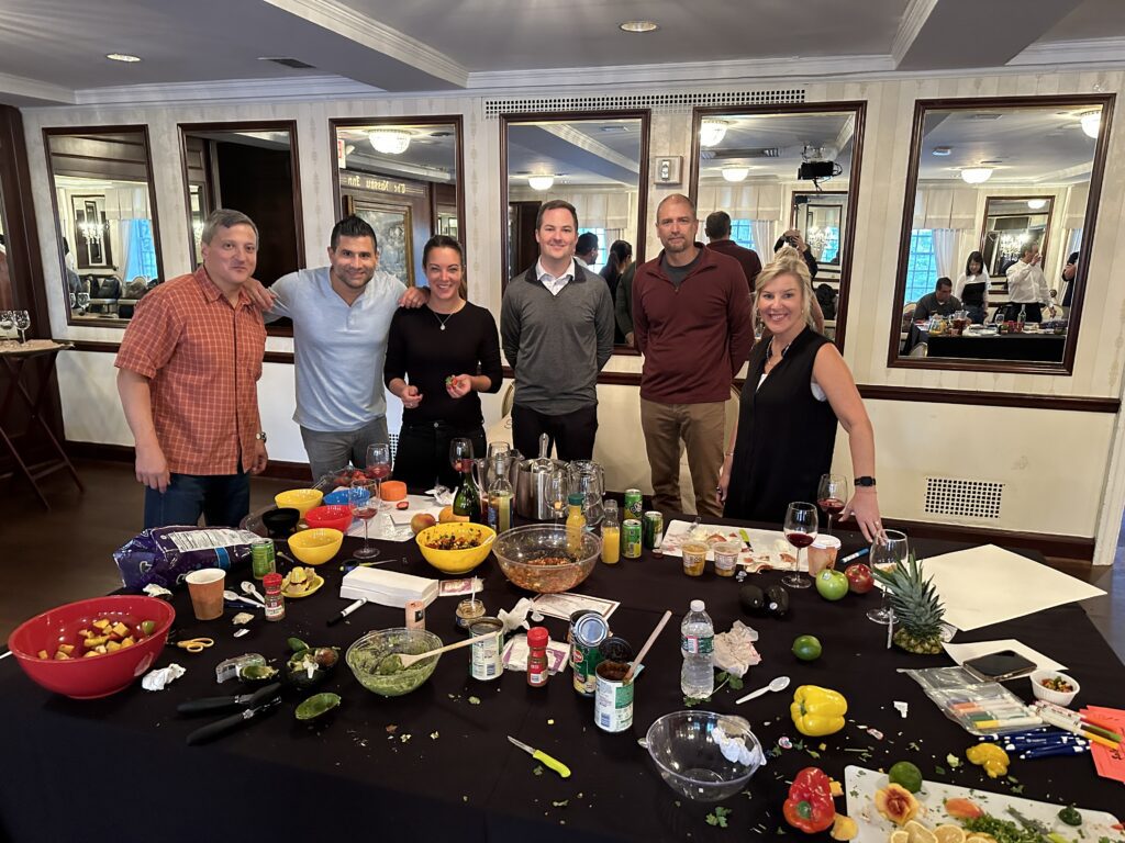 A team celebrating after completing the Salsa Showdown, surrounded by a variety of colorful ingredients, freshly made salsa, and drinks, showcasing the fun and competitive spirit of the event.