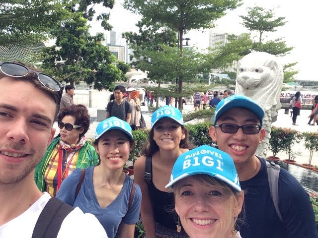 A group of smiling Go Give charity challenge participants posing for a selfie outdoors in front of a recognizable cityscape and landmarks. They seem to be enjoying the team building event.